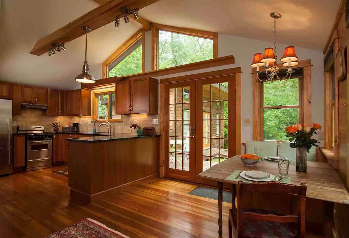 Open kitchen under a vaulted wood ceiling, french doors to the trees.