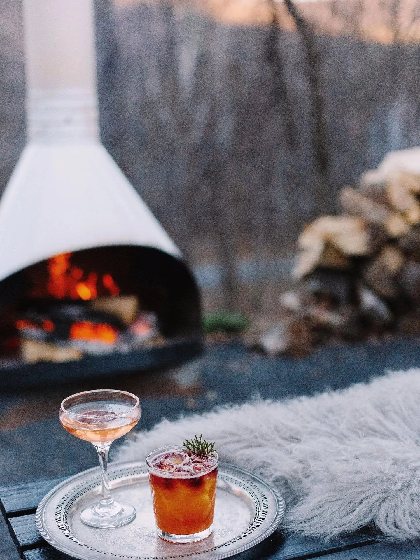 An outdoor hearth burning beside a low table with two cocktails.