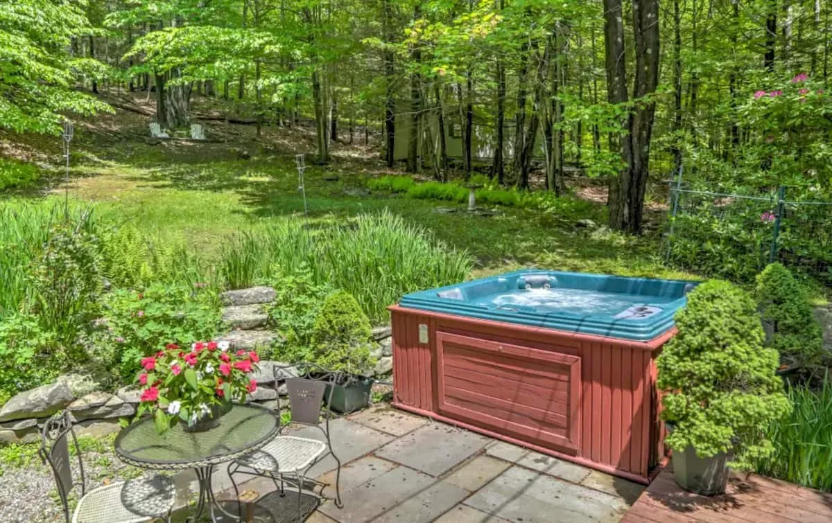 Hot tub on a stone patio, surrounded by ferns and trees.