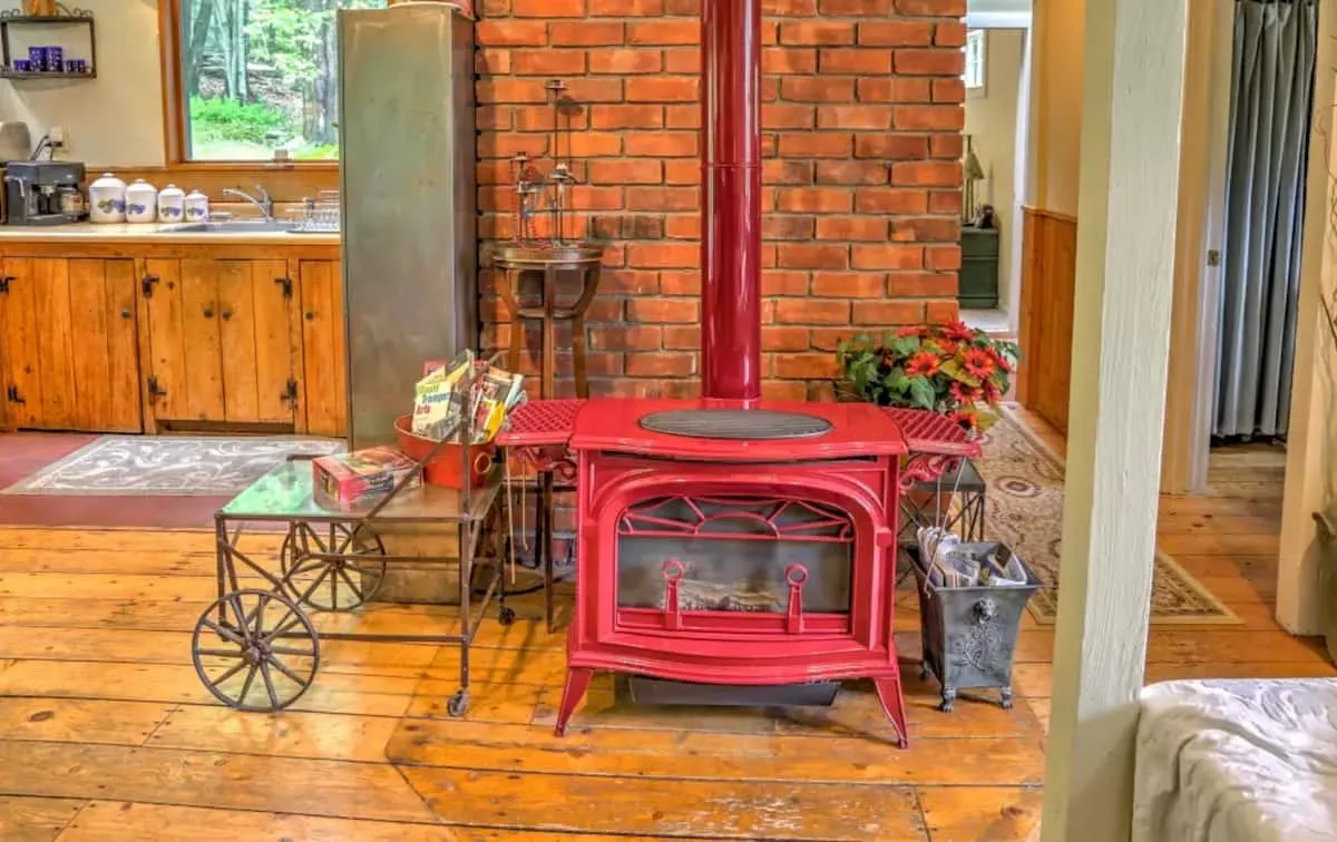 Red enamel wood stove against an exposed brick chimney.