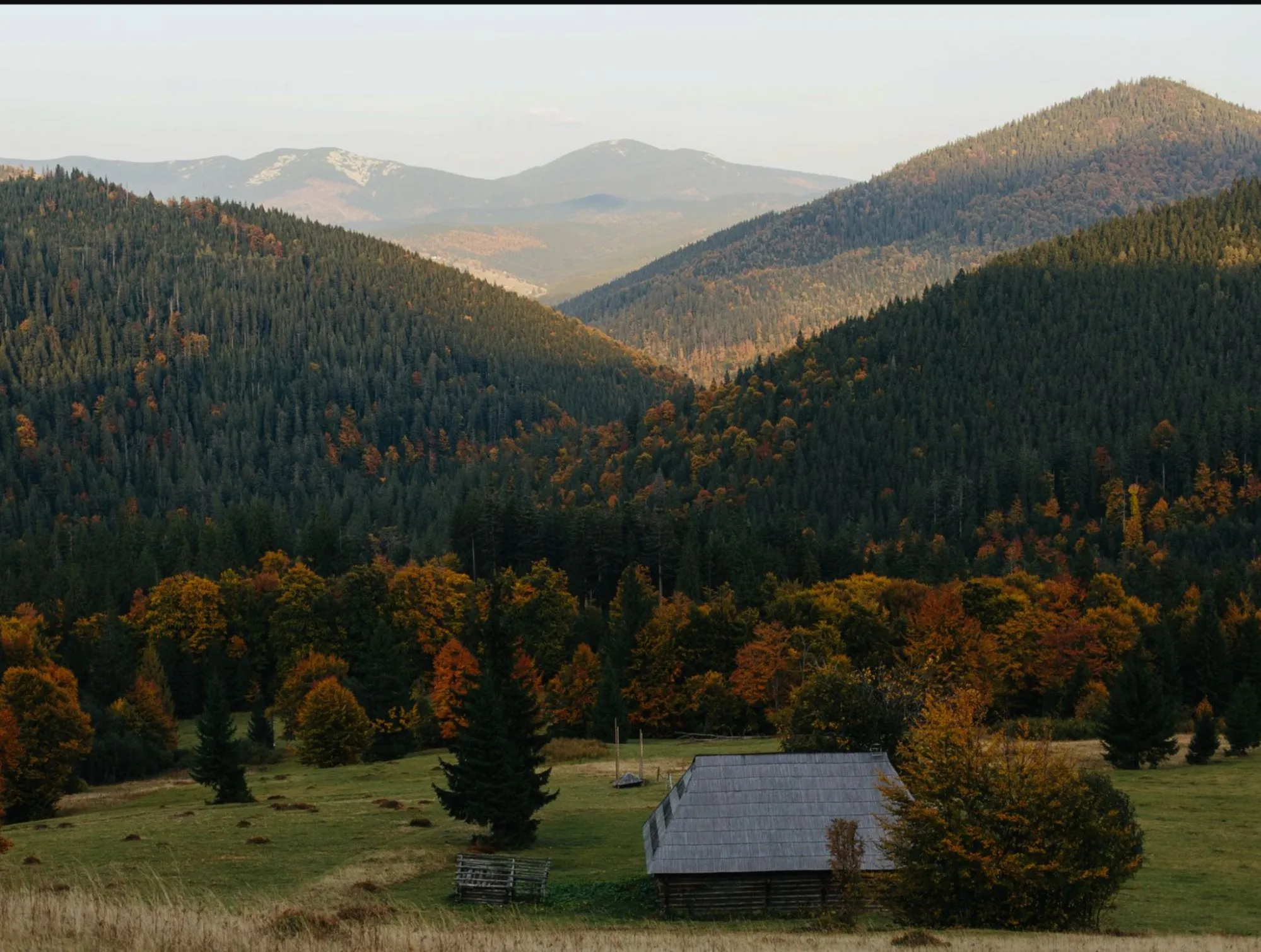 Ridgelines of the Catskills in autumn, a small cabin in the meadow below.